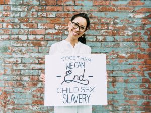 Picture of woman holding a sign that says "Together We Can End Child Sex Slavery"