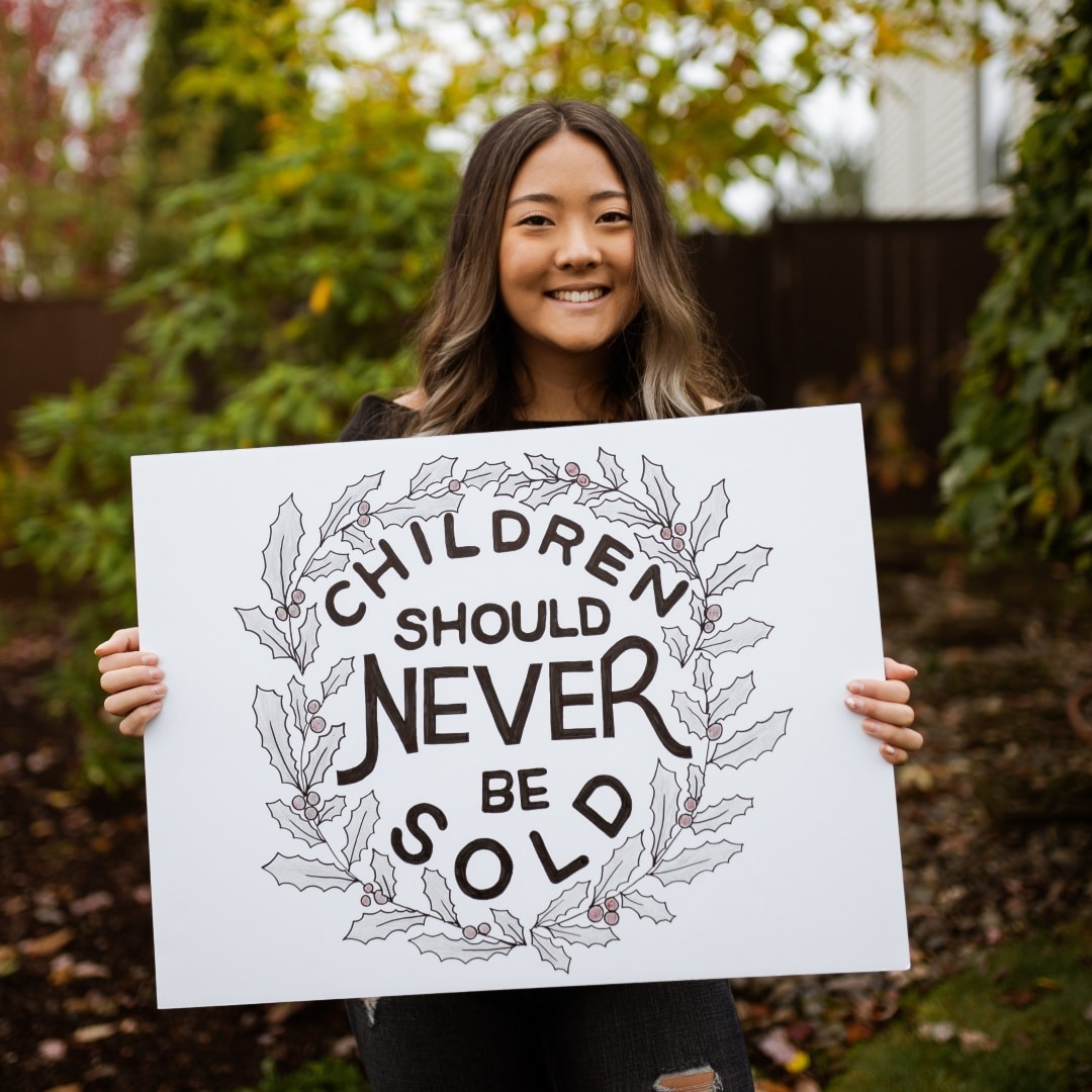 Girl holding a sign that says "Children should Never be sold"